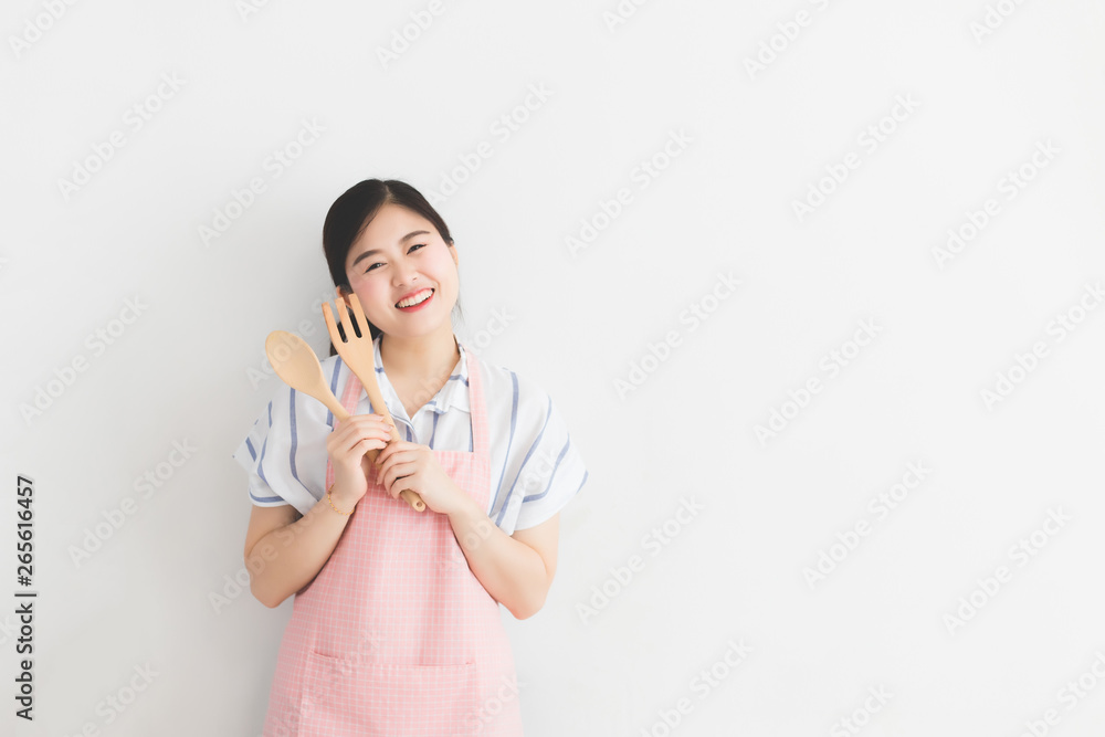 A young Thai woman, white skin, long hair, wearing a casual dress and pink apron, holding a kitchenware on a white wall in the morning in Thailand. with Copy Space A young Thai woman, white skin, long hair, wearing a casual dress and pink apron, holding a kitchenware on a white wall in the morning in Thailand. with Copy Space
