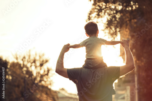 Obraz na plátně Happy family: Young father with his little child sitting on father's shoulders i