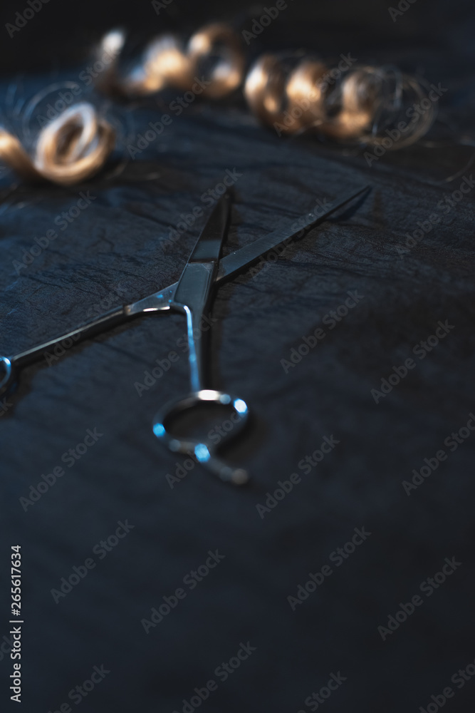 Piece of blonde curly hair and scissors on black fabric. Piece of blonde curly hair and scissors on black fabric.