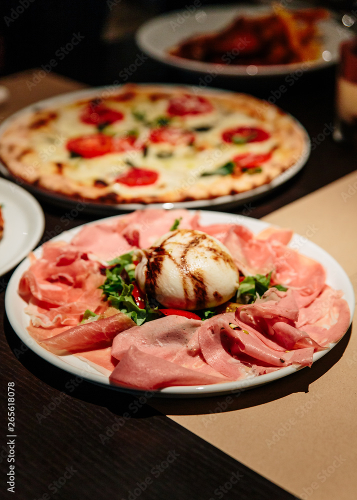 Cold Cuts Burratina: Burrata Cheese served with Parma Ham, Mortadella and Salad. Served in white plate on paper mat. Cold Cuts Burratina: Burrata Cheese served with Parma Ham, Mortadella and Salad. Served in white plate on paper mat.