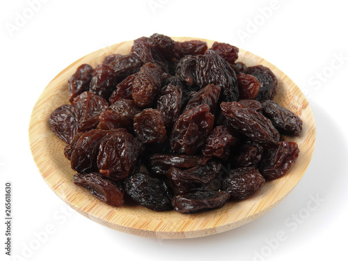 High angle view of raisins on wooden plate isolated on white background. A raisin is a dried grape. It tastes sweet and delicious. Texture detail of raisin surface. Food concept. With copy space.