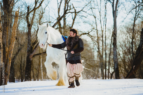 Man in suit of ancient warrior walking with the big white horse