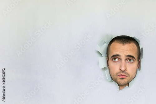 Sad man making hole in paper, looking up, grieving, blue background, copy space