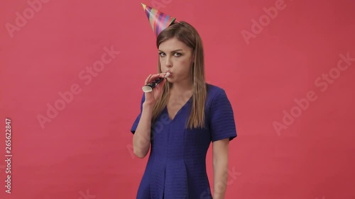 Sad girl in a festive hat, blowing a party whistle. Studio, purple background photo