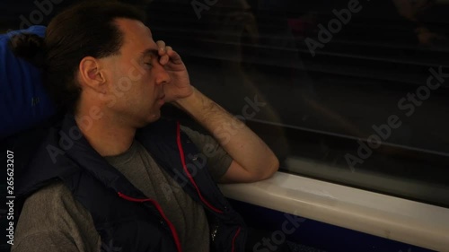 Man get some sleep wile travelling at regional train, portrait of passenger leaning to window with eyes closed. Late evening international journey photo