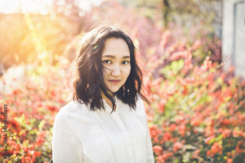 Cheerful asian young woman in a white blouse in a blooming park.