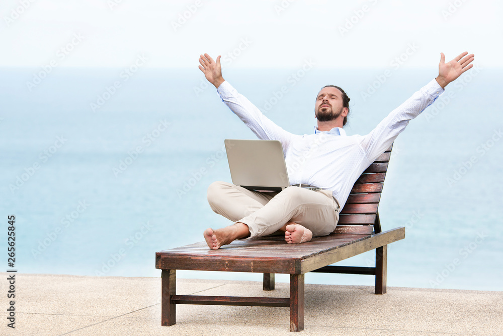Young businessman on the beach resting on his deck chair using his tablet