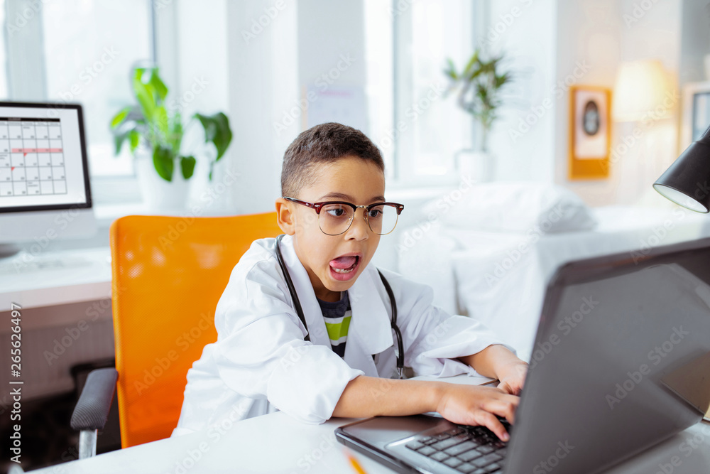 Funny boy putting out his tongue while using laptop of father at work Funny boy putting out his tongue while using laptop of father at work