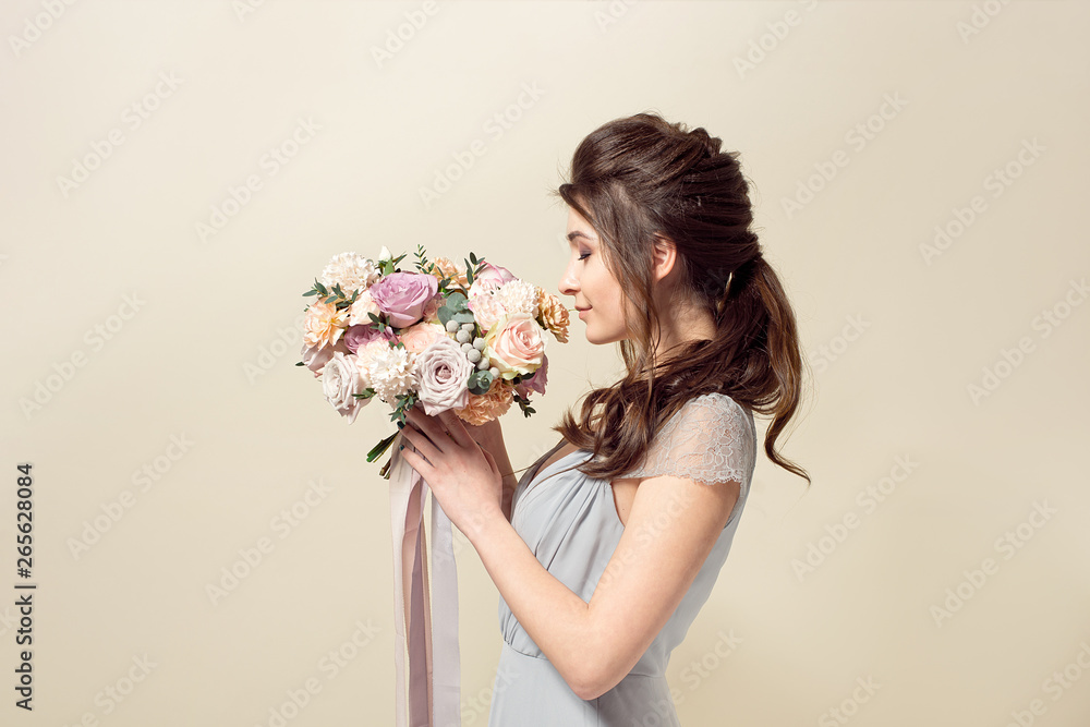 Elegant girl with a haircut in a soft blue dress and make-up is holding a bouquet of a stylish bouquet of flowers. Elegant girl with a haircut in a soft blue dress and make-up is holding a bouquet of a stylish bouquet of flowers.