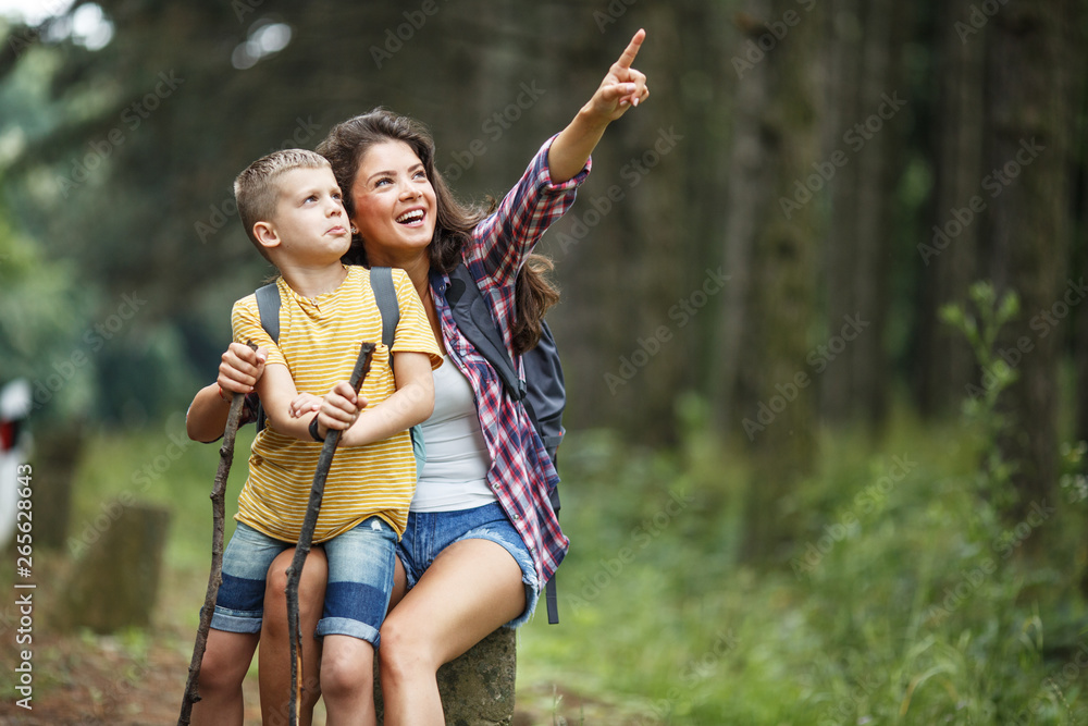 Fototapeta premium A mother and her little sons enjoy a hike in nature, pausing to rest on a rock by the roadside, soaking in the serenity of their surroundings.