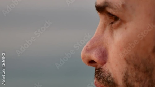 A profile closeup shot of eastern bearded young man look and blinks  Closeup Young bearded eastern man natural face looking and blinking at sandy beach at sunset 