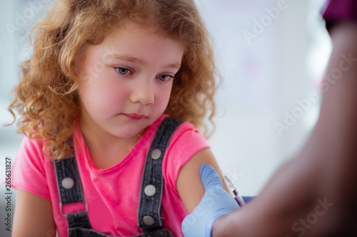 Blue-eyed curly girl having tears while getting injection photo