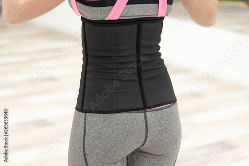 girl in black gray corset and sport leggings stands with a back half a turn to the viewer