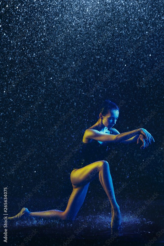 Young female ballet dancer performing under water drops and spray. Caucasian model dancing in neon lights. Attractive woman. Ballet and contemporary choreography concept. Creative art photo.