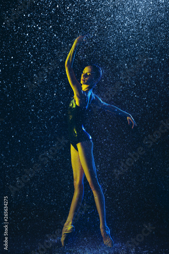 Young female ballet dancer performing under water drops and spray. Caucasian model dancing in neon lights. Attractive woman. Ballet and contemporary choreography concept. Creative art photo.