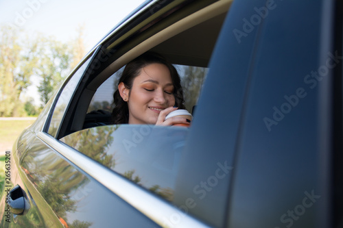 Businesswoman drinking coffee while riding in a backseat of a car © Daniel