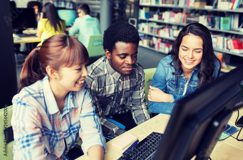 people, education, technology and school concept - group of happy smiling international students with computers at library in university