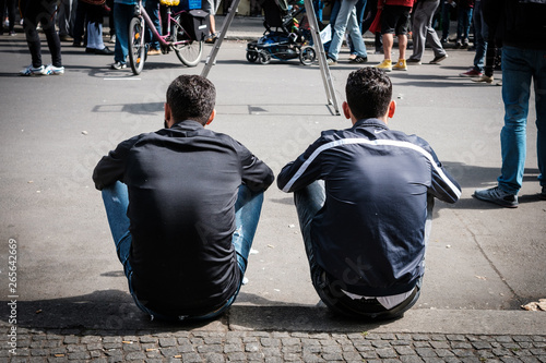 Photography Two men sitting on sidewalk from behind -