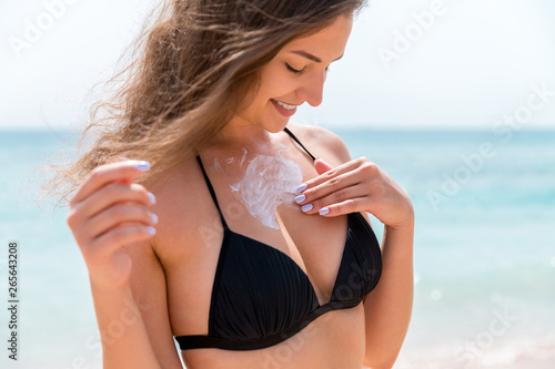 Young attractive woman is protecting her skin on the breast with sunblock at the sunny beach