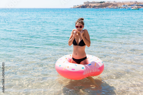 Young woman with inflatable ring cold shivering sad crossed arms black bikini swimsuit standing in sea water. Summer holidays and vacation concept
