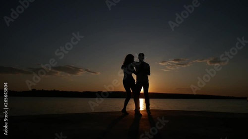 Young boy and girl dance salsa at sunset near the lake. Silhouette shooting. Slow motion