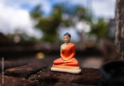 Cheap clay figurine of Buddha left on an old brick wall