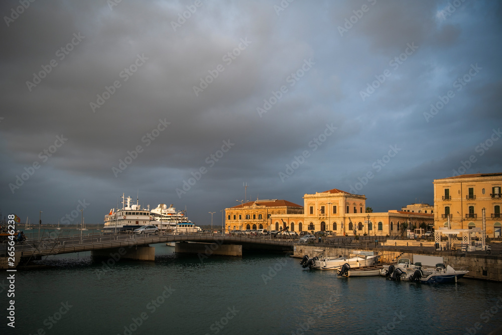 Bridge over the canal with boats and ships docked that joins Ortigia island and city of Syracuse in Sicily, Italy 