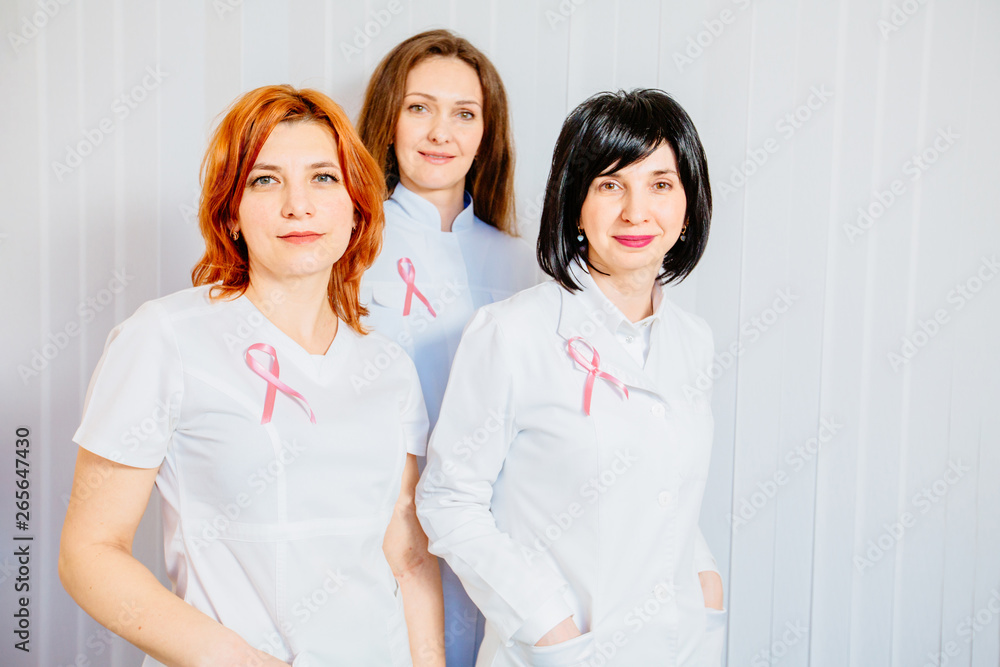 Confident nurses with pink ribbons smiling into camera, breast cancer awareness Confident nurses with pink ribbons smiling into camera, breast cancer awareness