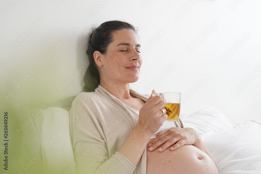 Pregnant woman laying on bed and drinking infusion Pregnant woman laying on bed and drinking infusion