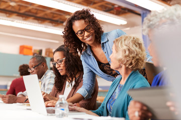 Teacher Helping Group Of Retired Senior Women Attending IT Class In Community Centre