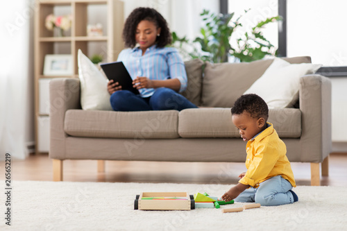 family, motherhood and people concept - african american baby playing with toy blocks kit and his mother using tablet computer at home
