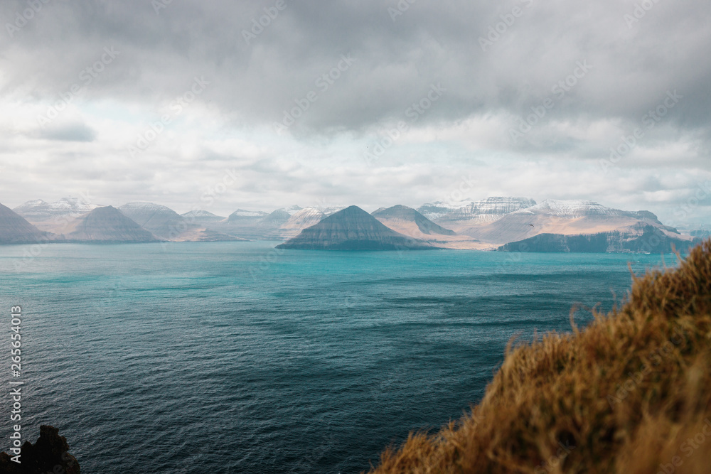 View from Kallur lighthouse on Kalsoy island towards the village of Gjógv on Eysturoy island with dramatic cloudy sky (Faroe Islands, Denmark, Europe) View from Kallur lighthouse on Kalsoy island towards the village of Gjógv on Eysturoy island with dramatic cloudy sky (Faroe Islands, Denmark, Europe)
