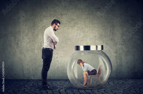 Slika na platnu Authoritarian boss businessman looking at a glass jar with captured woman inside