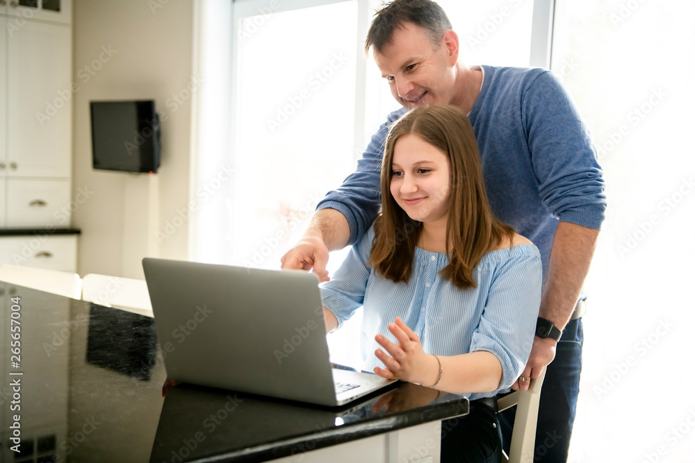A father using a laptop in kitchen with teenager A father using a laptop in kitchen with teenager