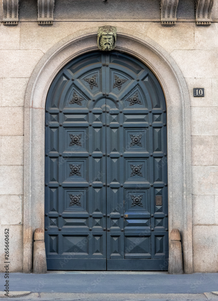 milan - italy, arched entrance in art nouveau style with floral decorations on the blue wooden door milan - italy, arched entrance in art nouveau style with floral decorations on the blue wooden door