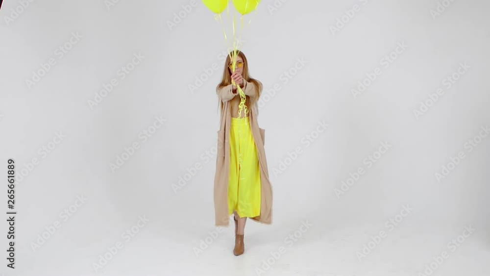 Girl in yellow skirt with yellow balloons in hands is posing at the camera at light background. Girl in yellow skirt with yellow balloons in hands is posing at the camera at light background.