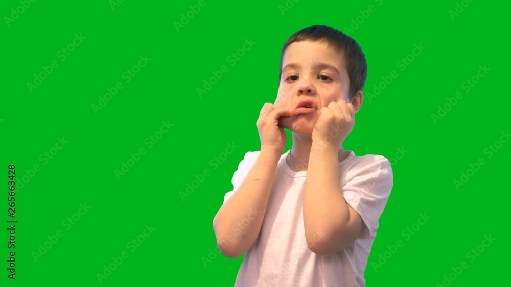 The boy stands on a green background. Hands stretches the face and makes a grimace. A child in a white t-shirt. Dark hair. 4K video. The boy stands on a green background. Hands stretches the face and makes a grimace. A child in a white t-shirt. Dark hair. 4K video.
