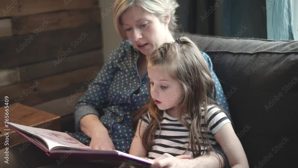 A mother teaching daughter holding book sitting on sofa A mother teaching daughter holding book sitting on sofa