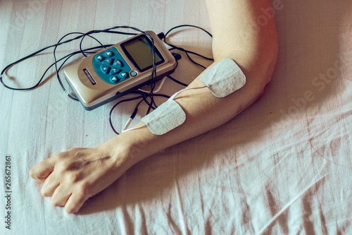 Small grey electro stimulator and white electrodes on a laying woman’s hand – Electric device used for massage and bodybuilding – Modern healthcare equipment for alternative therapies photo