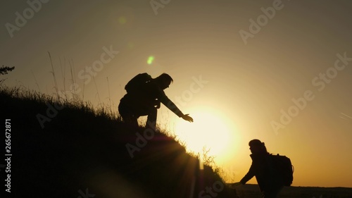 traveler man extends his hand to a girl climbing to the top of hill. travelers climb the cliff holding hand. teamwork of business people. Happy family on vacation. tourists hug on top of mountain