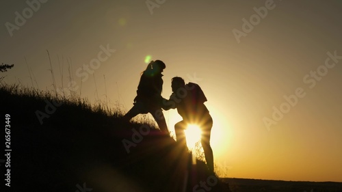 woman traveler stretches hand to man climbing to the top of a hill. travelers climb the cliff holding hands. teamwork of business people. Happy family on vacation. tourists hug on top of mountain