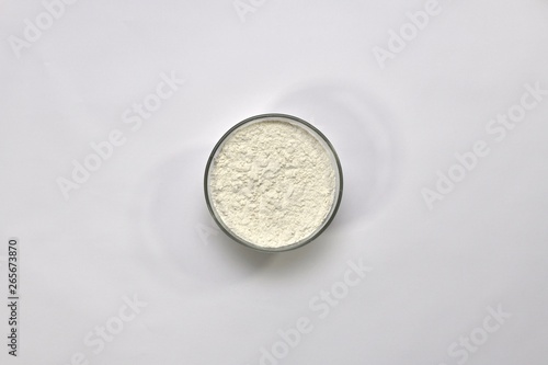 White wheat flour in a round cup on a light background. Top view, in the center.