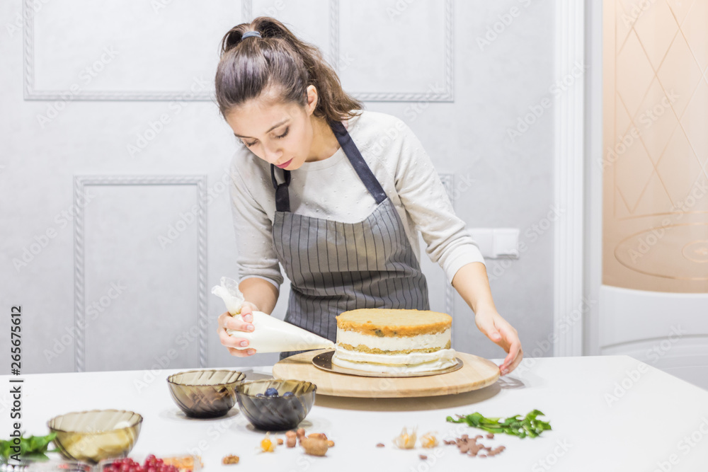 Confectioner with pastry bag squeezing cream on cake at kitchen. The concept of homemade pastry, cooking cakes.