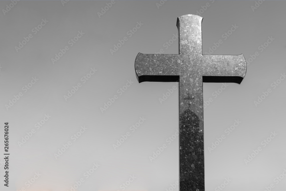 stone cross in a graveyard with copy space for text. crucifix against a gray background.