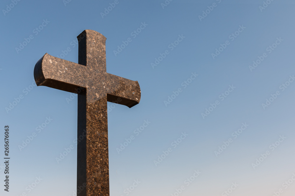 granite cross against the blue sky, copy space for text. Christianity faith and peace concept.