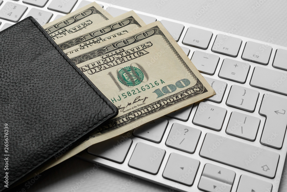 hundred dollar bills in a purse against a white computer keyboard. Fan of one hundred dollar bills in the wallet. purchase of goods and tickets via the Internet. hundred dollar bills in a purse against a white computer keyboard. Fan of one hundred dollar bills in the wallet. purchase of goods and tickets via the Internet.