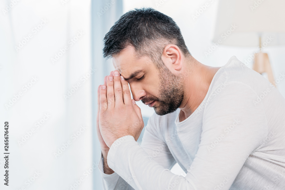 handsome bearded man with eyes closed doing please gesture and praying at home handsome bearded man with eyes closed doing please gesture and praying at home