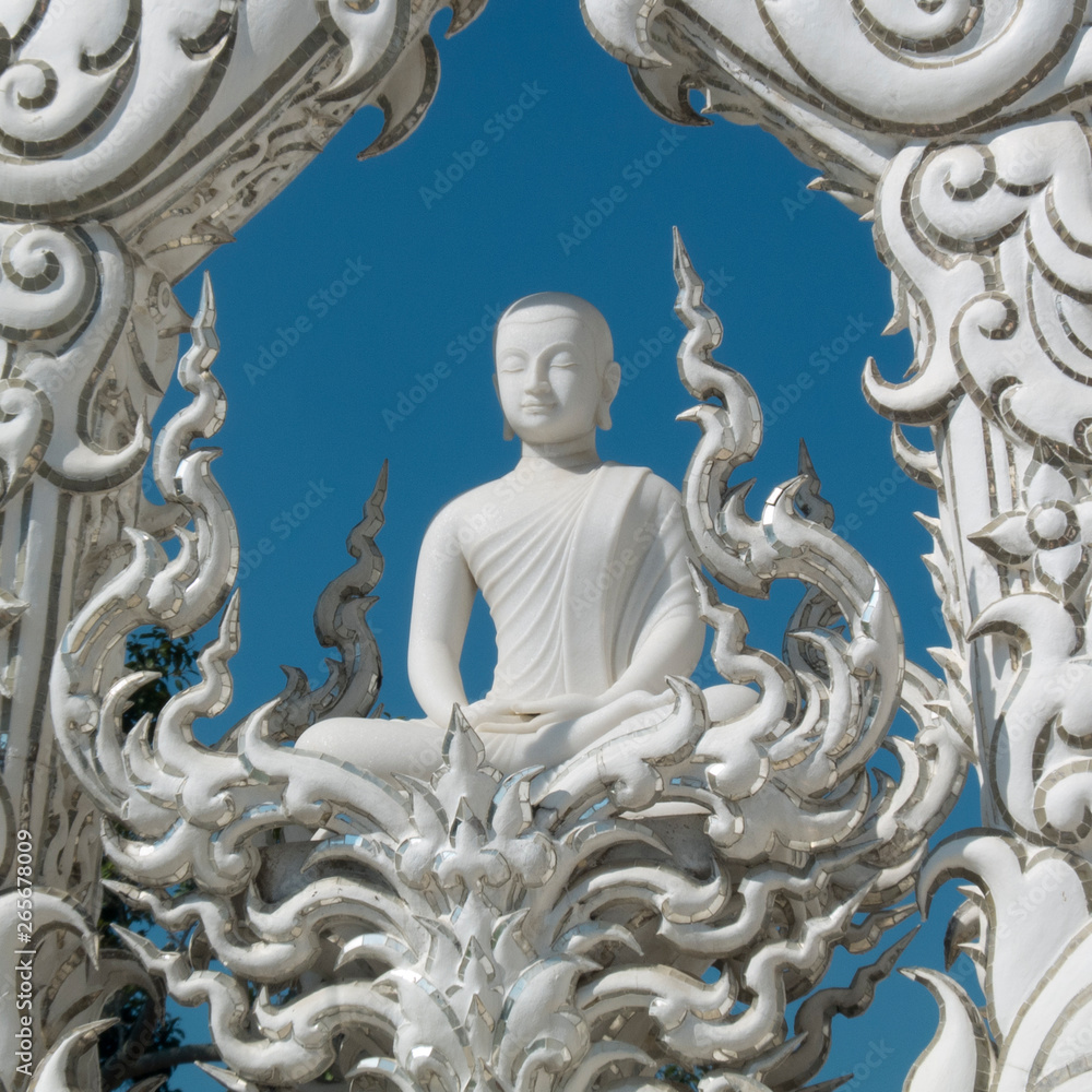 White temple, Wat Rong Khun in Chiang Rai, Thailand. White Buddha on a blue sky with his hands in the posture of meditation, serenity and calming . He closes his eyes to lifts his spirits.