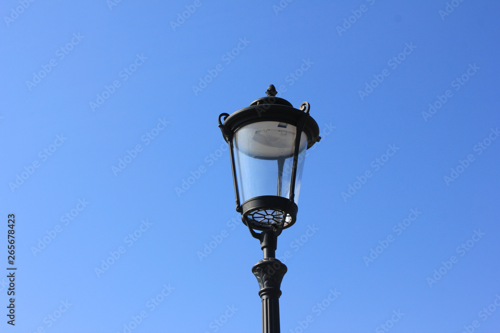 Old street lantern isolated on empty blue sky background. Retro lamp close up view