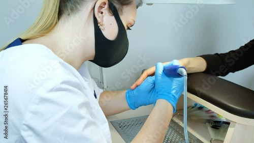 Girl manicurist in gloves cleans pterygiums from side rollers and cuticle hardware with flame cutter photo